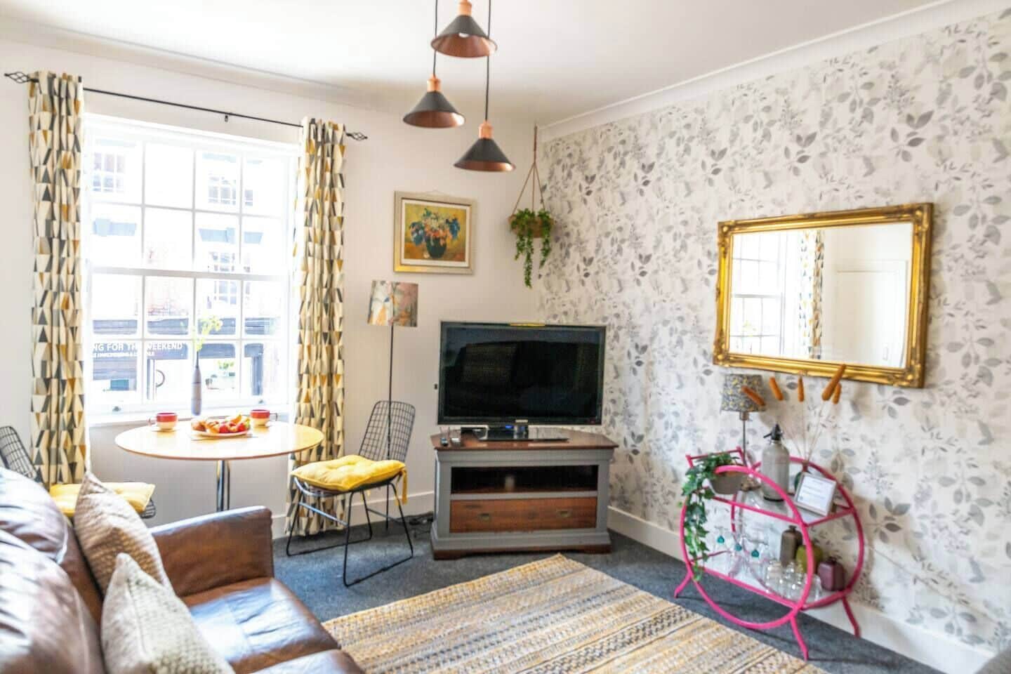 Een woonkamer met een bank, een televisie, een kleine tafel met stoel, een kamerbreed tapijt en een decoratieve spiegel.