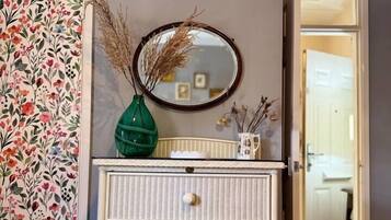 Una habitación con un aparador de mimbre blanco, un espejo y papel tapiz con motivos florales.