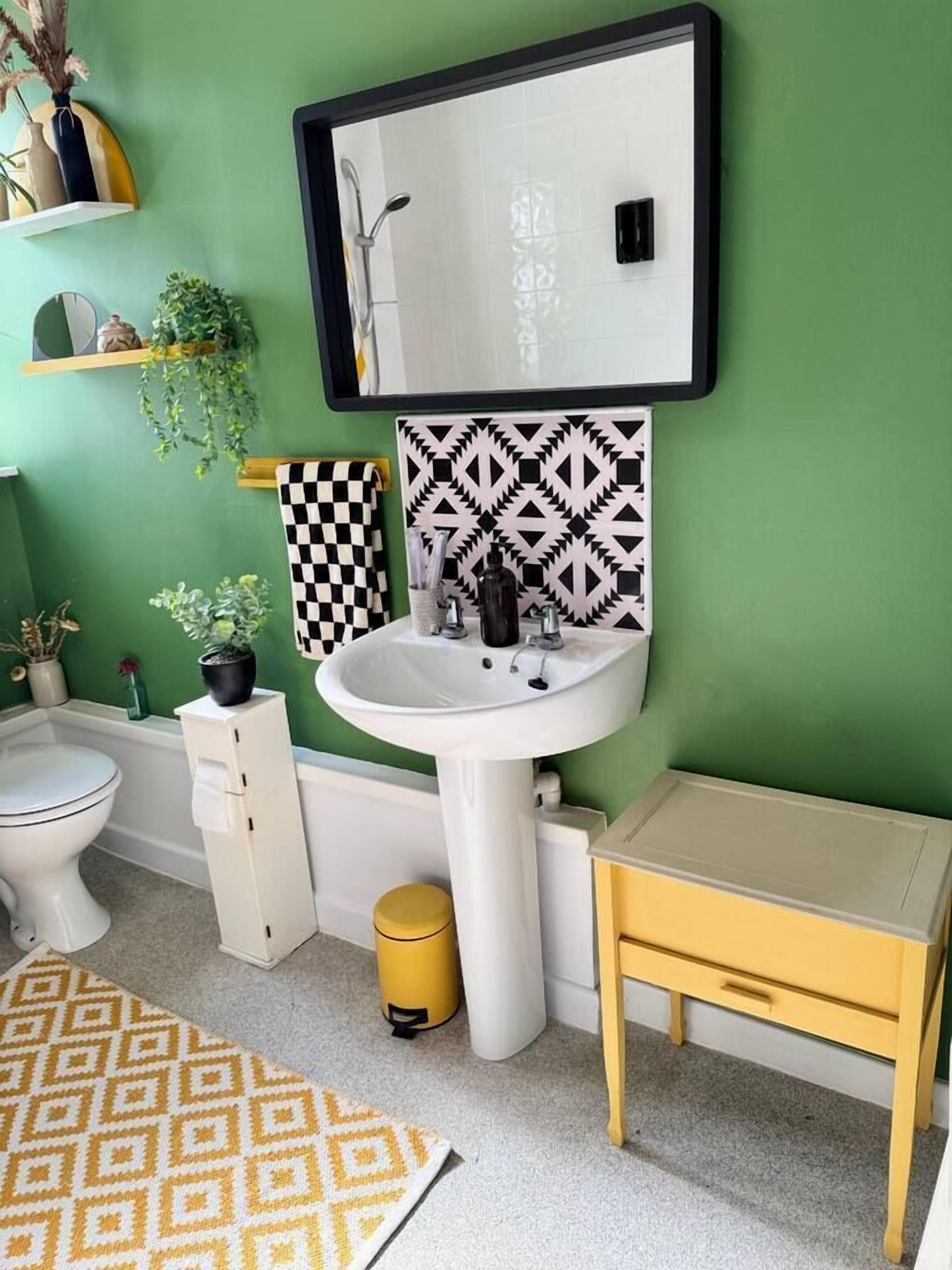 Un baño con un lavamanos blanco, un espejo, un inodoro y un cubo de basura amarillo.