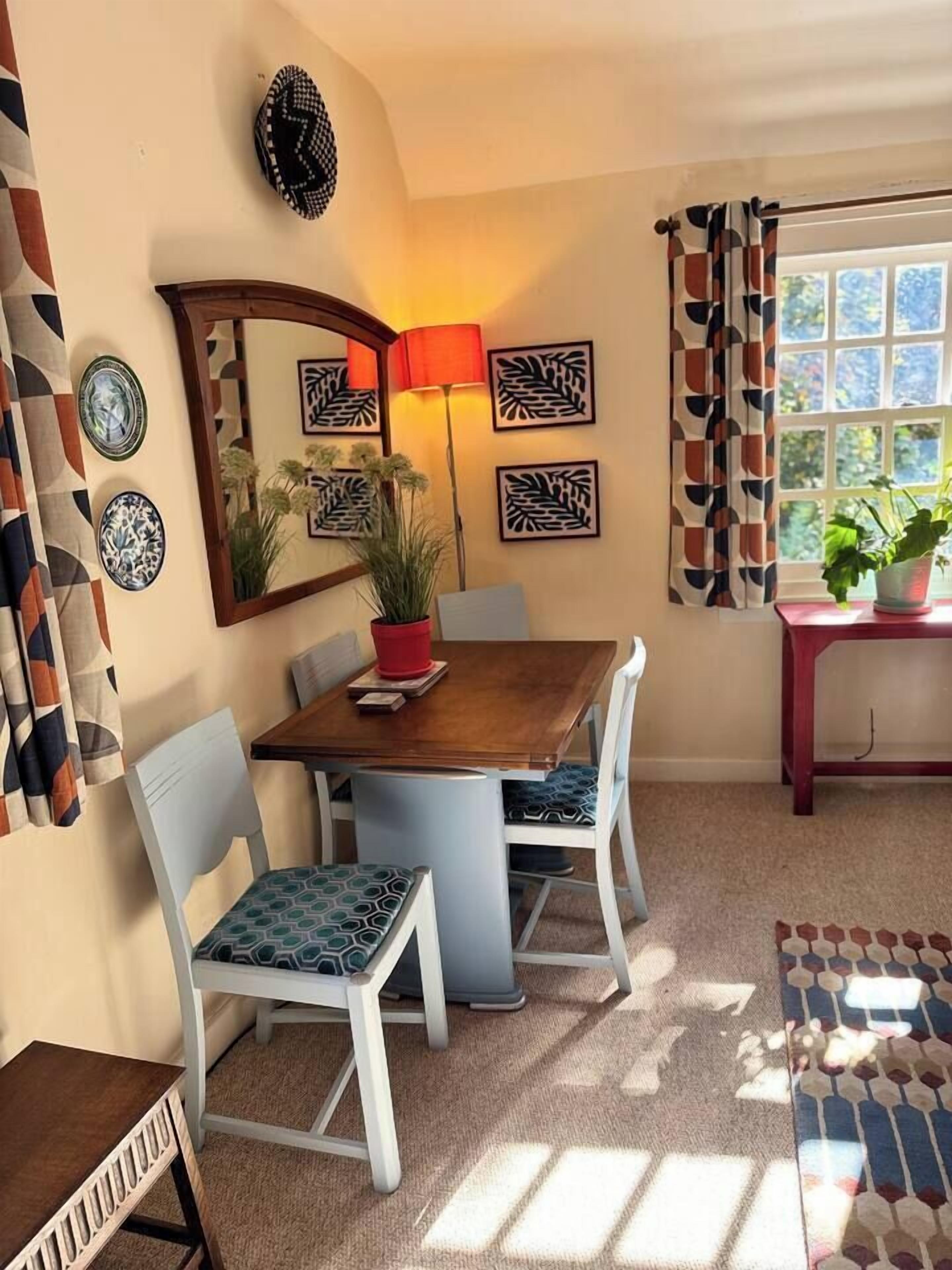 Un comedor con una mesa de madera, sillas blancas, una lámpara roja y decoración en la pared.