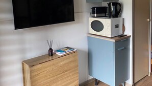 Quarto com televisão de tela plana na parede, micro-ondas em um pequeno armário, cômoda de madeira e uma porta.