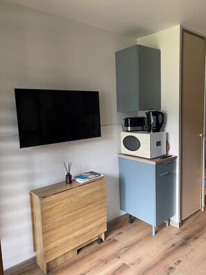 Ein Zimmer mit flachbildfernseher an der Wand, einer Mikrowelle auf einem kleinen Schrank, einem hölzernen Kommode und einer Tür.