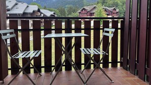 Varanda com duas cadeiras e uma mesa, com vista para uma paisagem montanhosa com casas.