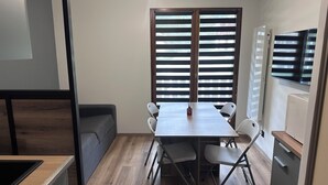 Um espaço compacto com cozinha compacta, uma mesa de jantar com cadeiras, um sofá e uma televisão fixada na parede.