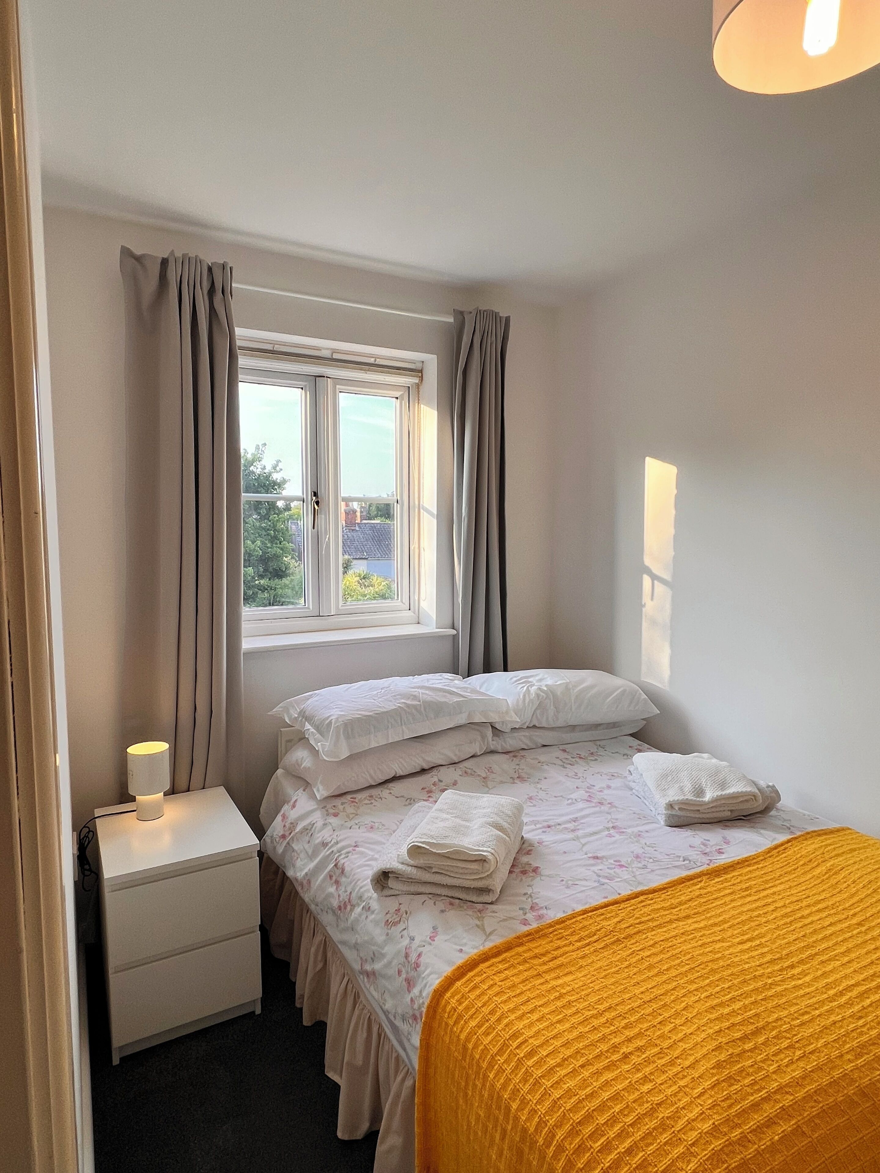 Un dormitorio con cama, mesita de noche, ventana con cortinas y vista al exterior.