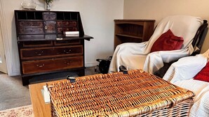 Quarto com um banquinho de vime, um armário de madeira, uma cadeira e uma cama.
