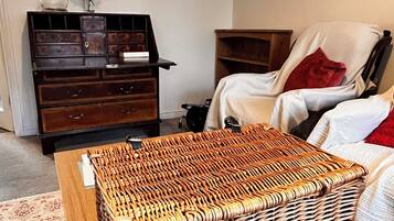 A room with a wicker ottoman, a wooden cabinet, a chair, and a bed.