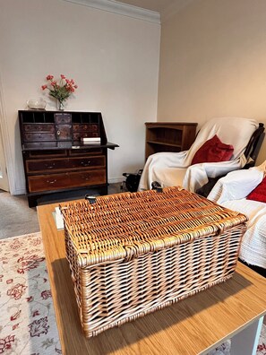 Ein Zimmer mit Hocker aus Weidengeflecht, einem Holzschrank, einem Sessel und einem Bett.