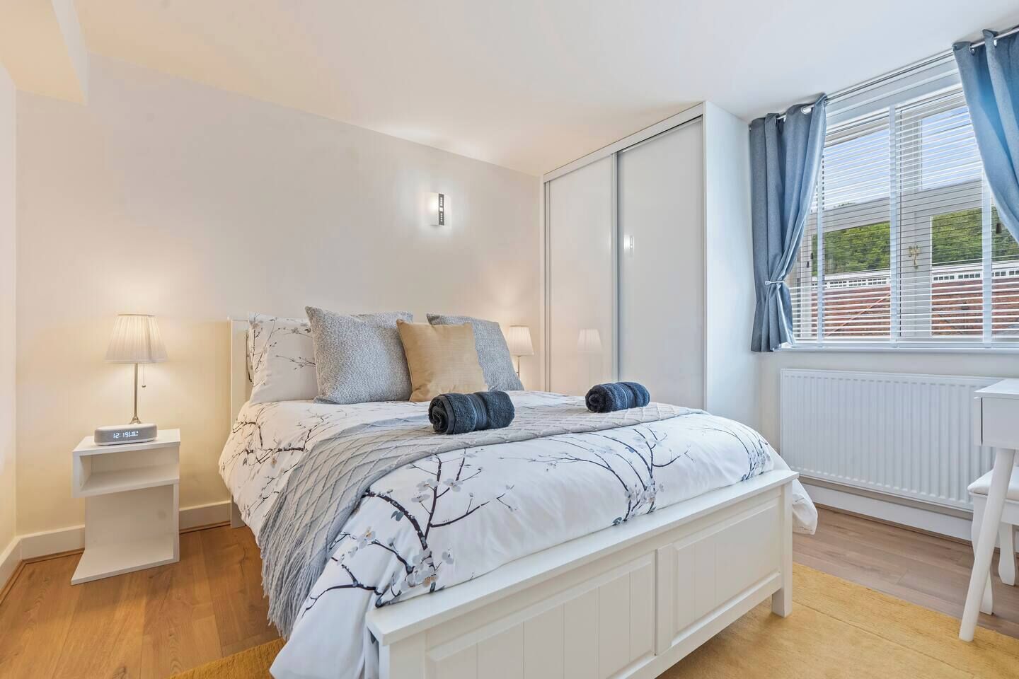 Een slaapkamer met een bed, nachtlampen, een raam met gordijnen en uitzicht.