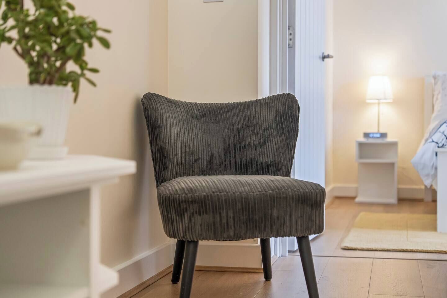 Ein moderner Stuhl mit Rippenmuster, platziert in einem gut beleuchteten Zimmer mit Holzboden, einem Nachttisch und einer Lampe.