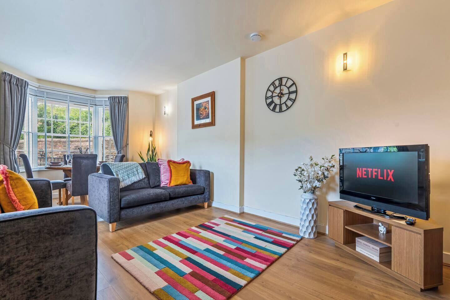 A modern living room with a sofa, a television displaying 'NETFLIX,' a clock, and a window with curtains.