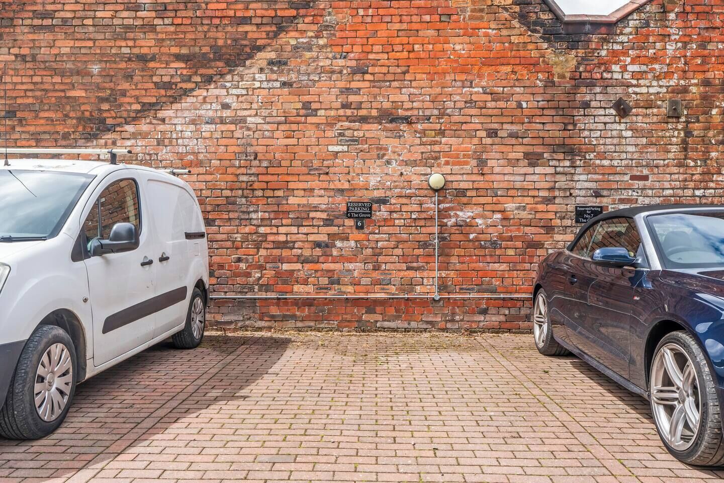 Two cars parked in front of a brick wall with a sign indicating reserved parking.