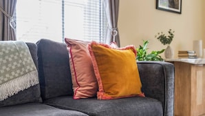 Un canapé gris avec trois coussins de couleurs différentes et un plaid vert à motifs.