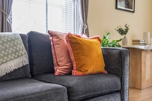 Ein graues Sofa mit drei Kissen in verschiedenen Farben und einer grünen, gemusterten Decke.