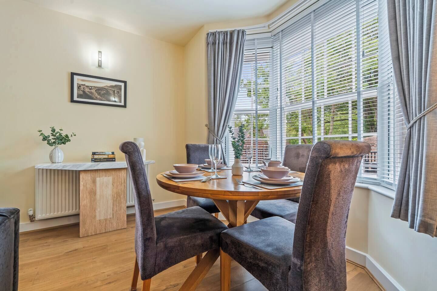 A dining area with a round table, chairs, and a window with blinds.
