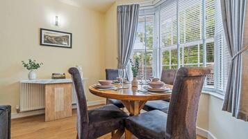 A dining area with a round table, chairs, and a window with blinds.