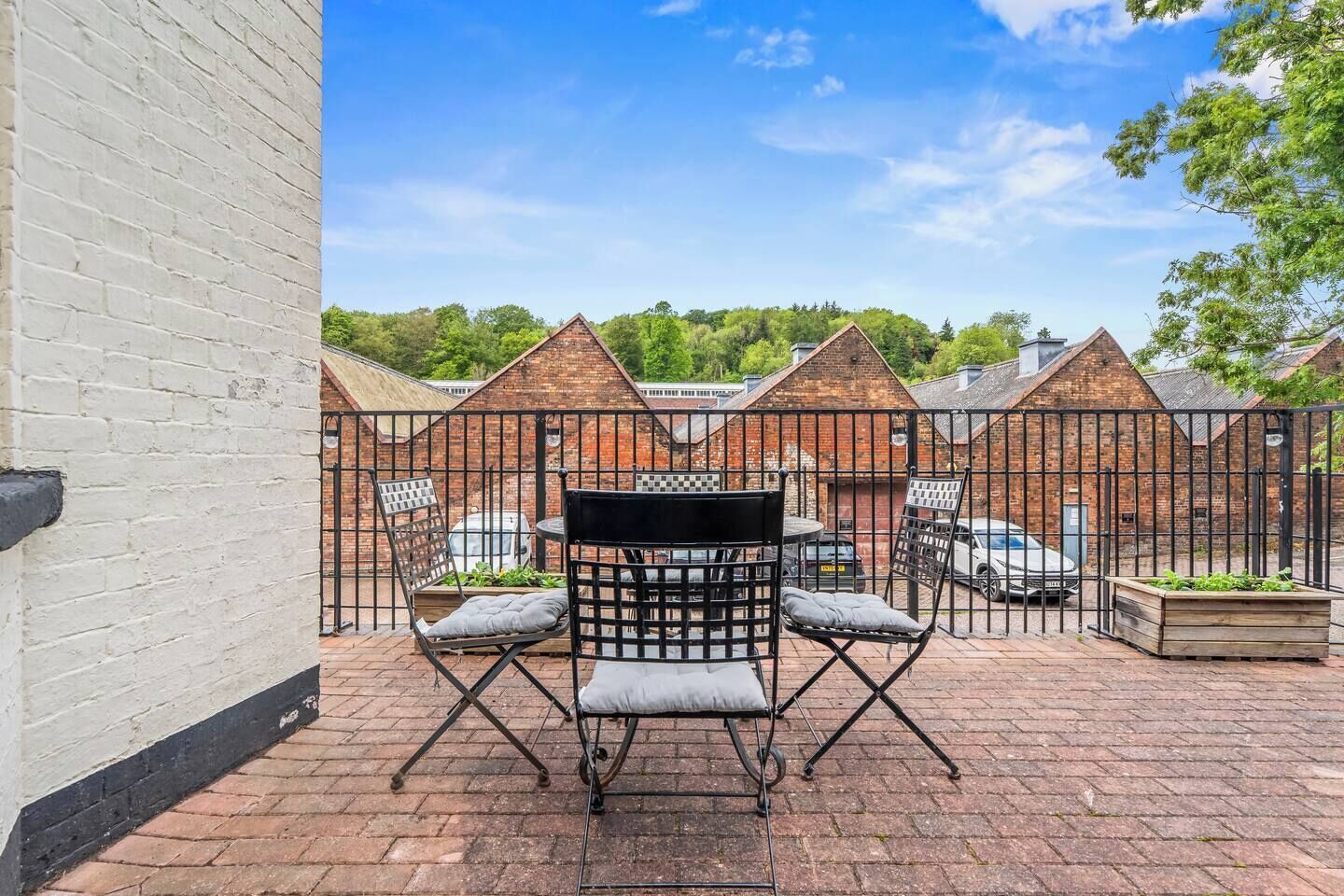 A patio with a table and chairs, a brick wall, and a view of a brick building with a fence.
