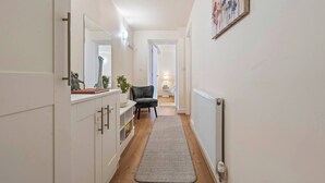 Un couloir étroit avec un radiateur, une chaise et une plante.