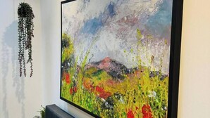 Ein Gemälde mit einem Neonzeichen darüber, einer hängenden Pflanze und einem Sofa mit Kissen.