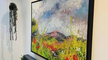 A painting with a neon sign above it, a hanging plant, and a sofa with cushions.