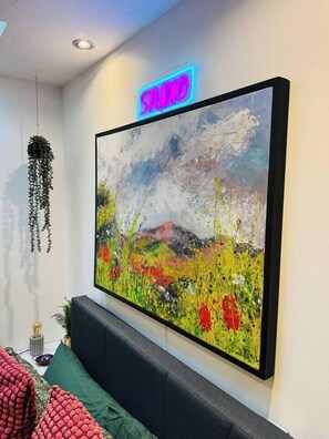 A painting with a neon sign above it, a hanging plant, and a sofa with cushions. - #11 Spacious Studio|Sleeps 4|5mins CannonHillPark (West Midlands)