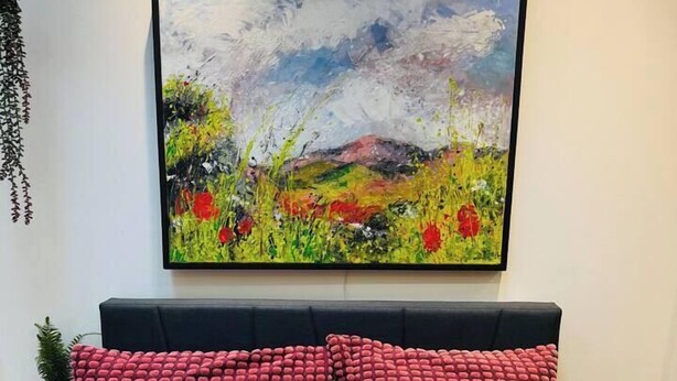 Ein Schlafzimmer mit einem Bett, roten Kissen, einem farbenfrohen Kissen, einem Gemälde und einer Neonreklame.