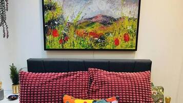A bedroom with a bed, red pillows, a colorful pillow, a painting, and a neon sign.