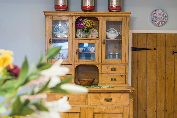 Um armário de madeira com portas de vidro, contendo diversos pratos e um vaso com flores.