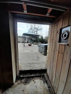 Uma porta de entrada dá para uma área externa com estrutura coberta, hidromassagem e lixeira.