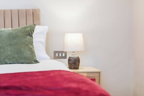 A bed with a green pillow, white pillow, and red blanket. There is a nightstand with a lamp and a power outlet. - #110 Charming Country Stay at Brook Farm, Somerset (Whatley)