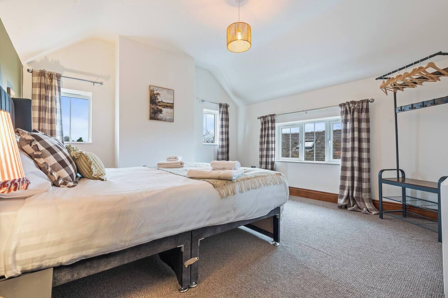 A bedroom with a bed, a window, a painting, and a hanging light fixture.