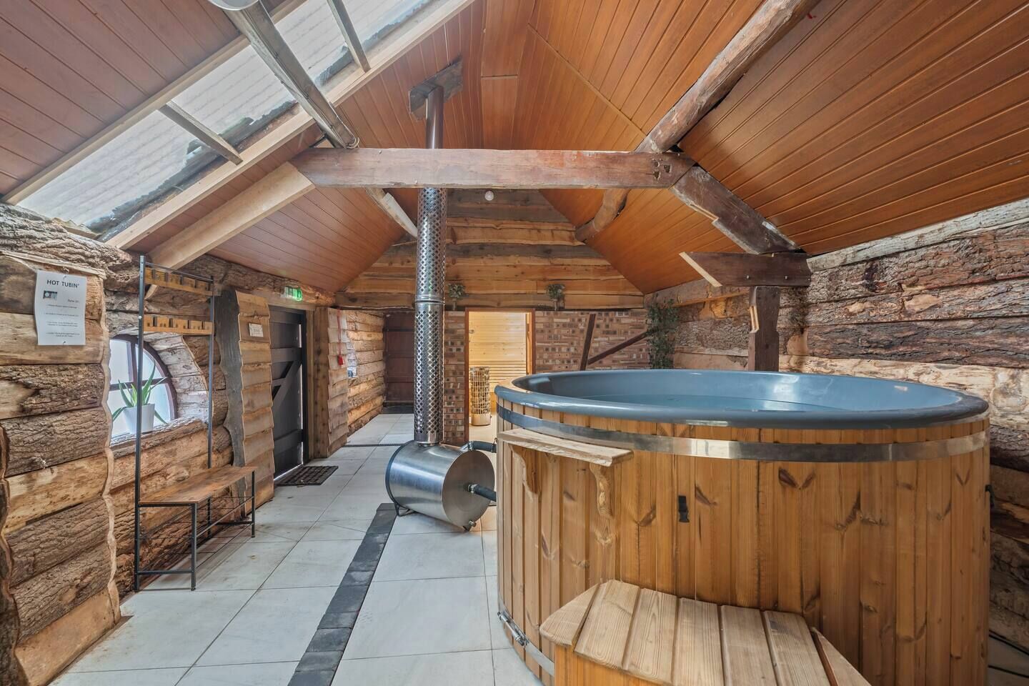 Interior de una cabaña de troncos con un jacuzzi, una chimenea de metal y un tragaluz.