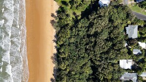 An aerial view of a beach with waves, dense greenery, and residential buildings.