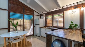 A modern kitchen with wooden cabinetry, a white refrigerator, and a dining area with a round table and stools.