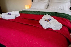 A hotel bed with a red bedspread, two rolled white towels with a Haribo logo, and a white pillow.