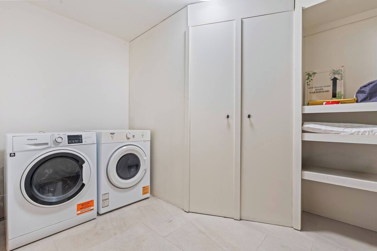 A laundry room with two front-loading washing machines, a white wardrobe, and a shelf with folded clothes.