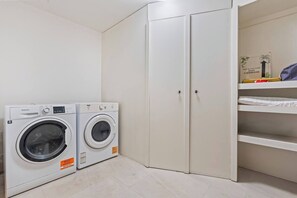A laundry room with two front-loading washing machines, a white wardrobe, and a shelf with folded clothes.