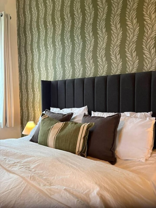 A neatly made bed with a variety of pillows and a headboard against a patterned wallpaper.