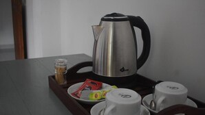 Eine Kaffeemaschine aus Edelstahl auf einer Tablett, mit zwei weißen Tassen, einer kleinen Zuckerdose und Sahneportionen.