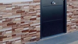 Una puerta negra con un detalle de pared de piedra, un letrero con el logotipo de una 'V' roja y un cartel con el número '3'.