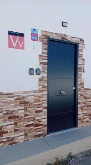 Eine schwarze Tür mit Steinwand und einem Schild mit dem roten 'V'-Logo sowie einem Schild mit der Nummer 3.