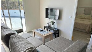 Una sala moderna con un sofá, una mesa de centro, un televisor y una cama al fondo.