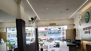 Zona de recepción de un hotel con suelo de baldosas, un mostrador de recepción, un reloj de pared y vistas a la calle.