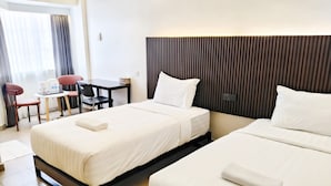 Habitación de hotel con dos camas, un escritorio, una silla y una ventana con cortinas.