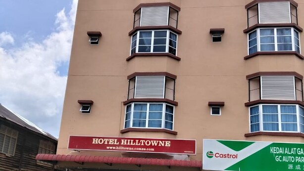 Un edificio de hotel con un cartel que dice 'Hotel Hilltowne' y una estación de servicio Castrol al frente.