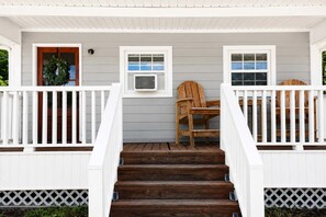 A wooden staircase leading to a porch with white railings and a wooden chair.