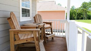Un terrazza in legno con poltrone Adirondack e un tavolo, ringhiere bianche e una casa sullo sfondo.