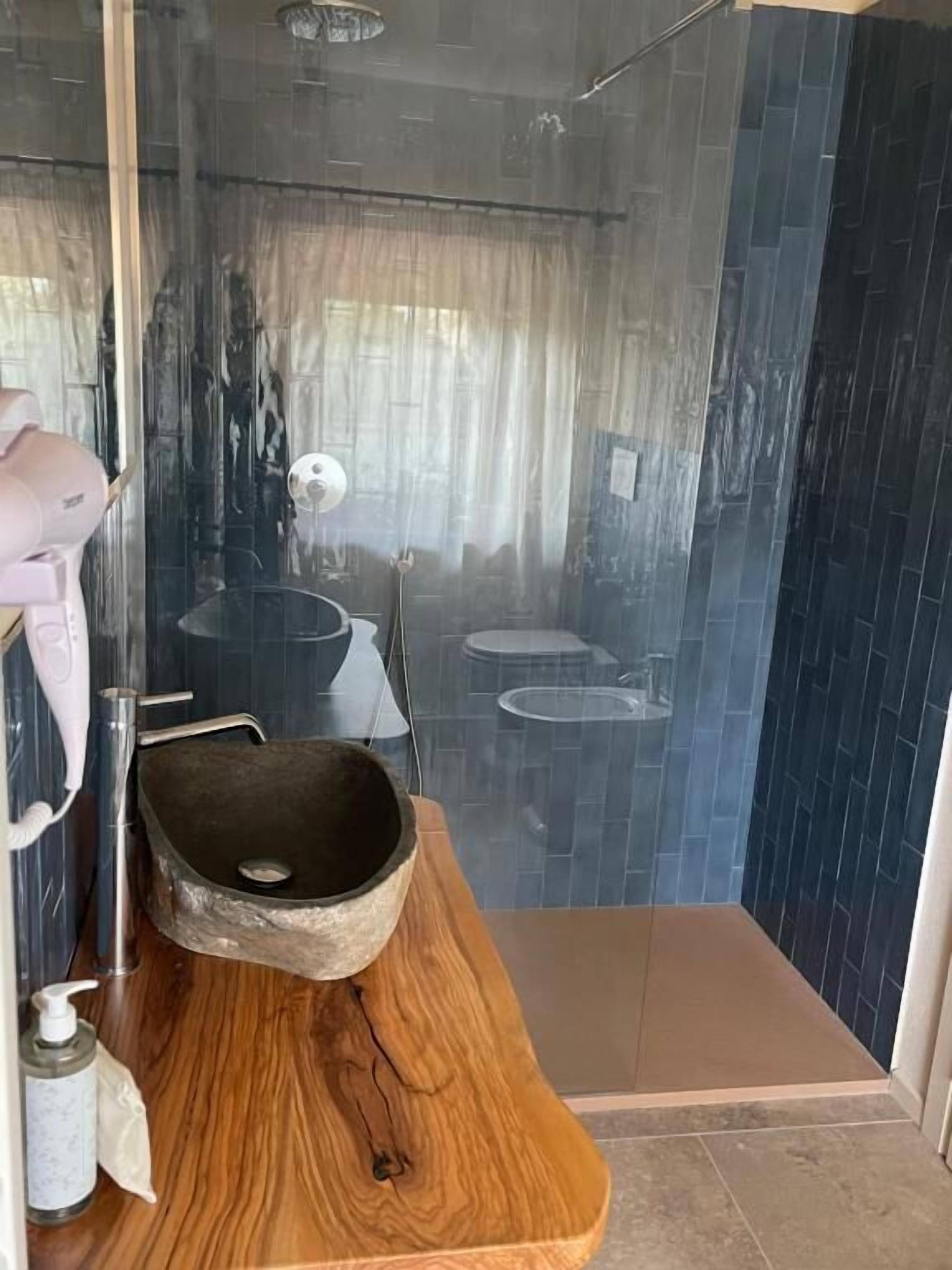 Une salle de bain avec un meuble-lavabo en bois, un évier en pierre et une cabine de douche en verre.