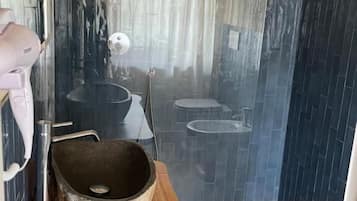 Une salle de bain avec un meuble-lavabo en bois, un évier en pierre et une cabine de douche en verre.
