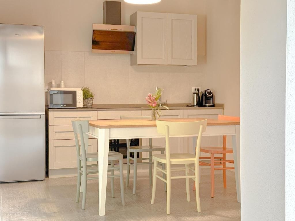 Una cocina equipada con refrigerador, microondas, gabinetes, cafetera y una mesa con sillas.